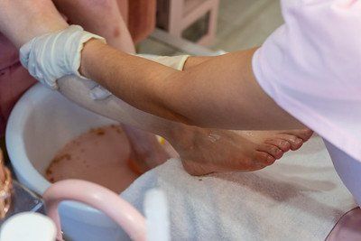 A person's foot being soaked in a foot spa by a gloved hand in a salon.