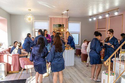 Women in navy robes at a bridal party in a bright, pink-accented salon.