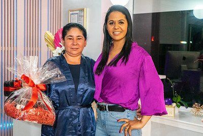 Two women smiling, posing near a gift basket in a beauty salon. One wears blue, the other magenta.