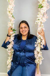 Woman in blue outfit smiles on a floral swing, with glasses.