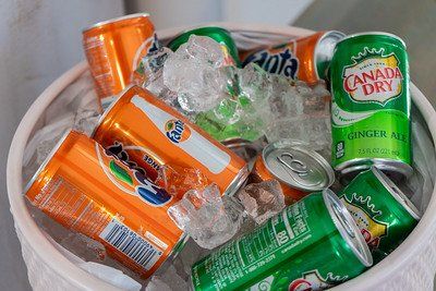 Orange Fanta and green Canada Dry soda cans in a white bucket filled with ice.