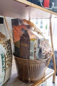 Gift basket in a brown metal container, wrapped in cellophane on a shelf.