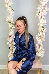 Woman in navy robe, smiling, sitting on a pink swing decorated with flowers.