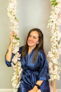 Woman in blue robe on a floral swing, smiling.