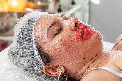 Woman with red lip mask and hairnet, lying on a massage table.