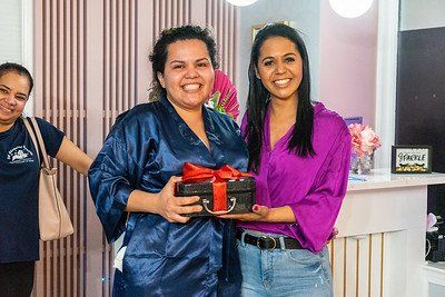 Two women smiling, one holding a gift box. Setting: a beauty salon.