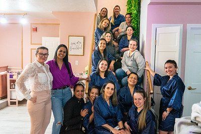 Group of women in robes on stairs, smiling for a photo in a pink and white room.