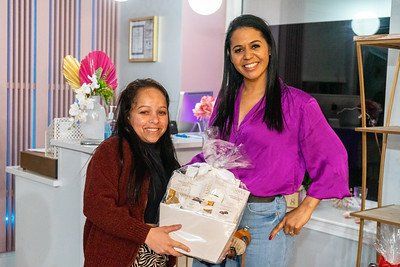 Two smiling women, one holding a gift basket. The setting appears to be a business with colorful decor.