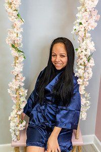 Woman in navy blue pajamas smiles, sitting on a pink swing decorated with pink flowers.