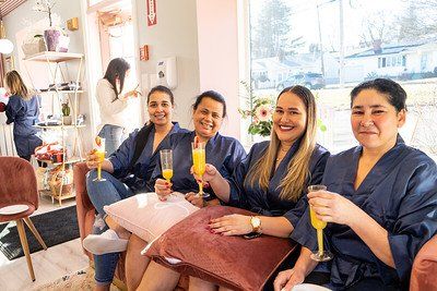 Four women in robes smiling, toasting with mimosas in a salon setting.