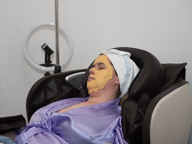 A woman is laying in a chair with a yellow mask on her face.