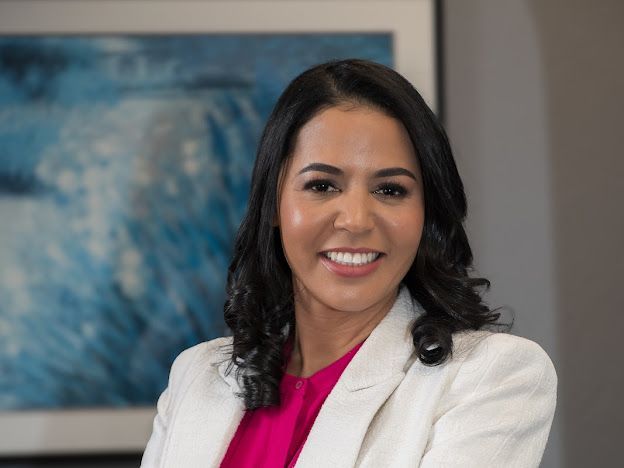 A woman in a white jacket and pink shirt is smiling for the camera.