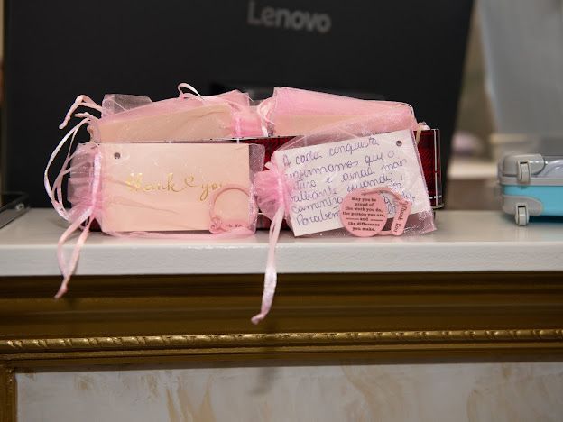 A lenovo laptop is sitting on a table next to a box of pink gifts.