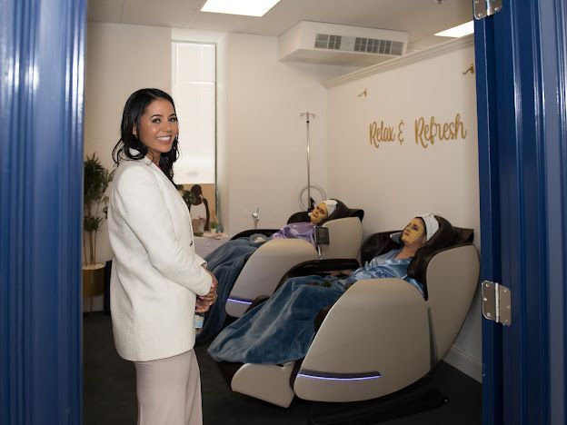 A woman is standing next to a woman laying in a massage chair.