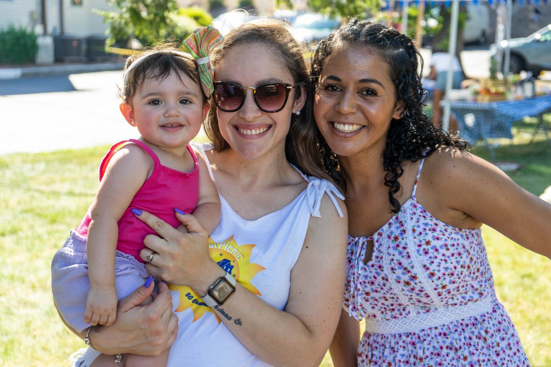 Woman holding toddler smiles with another woman outdoors.