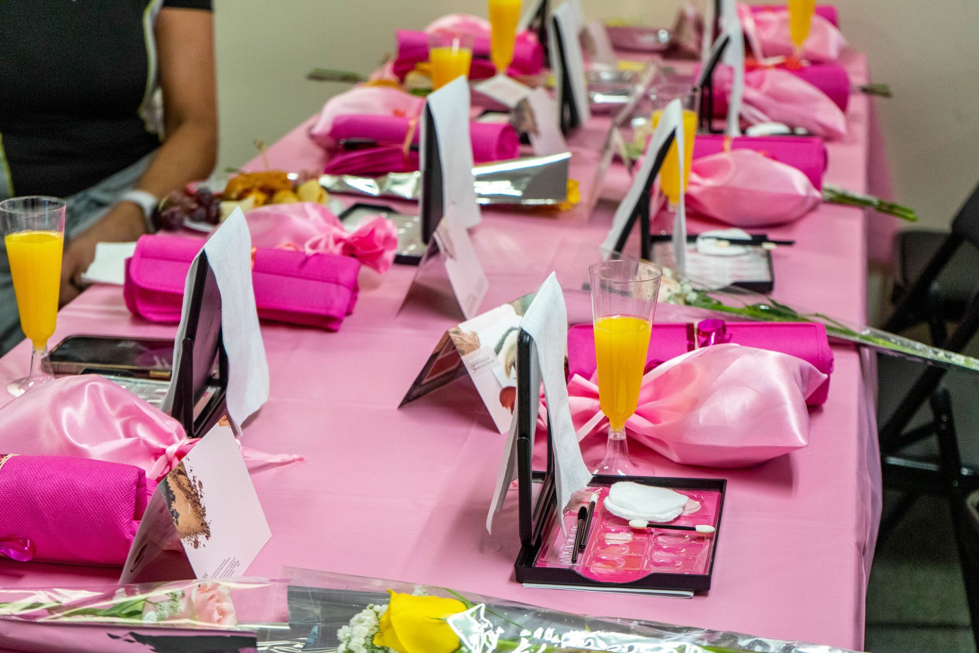 Pink-themed table setting: makeup, gifts, drinks, and flowers.