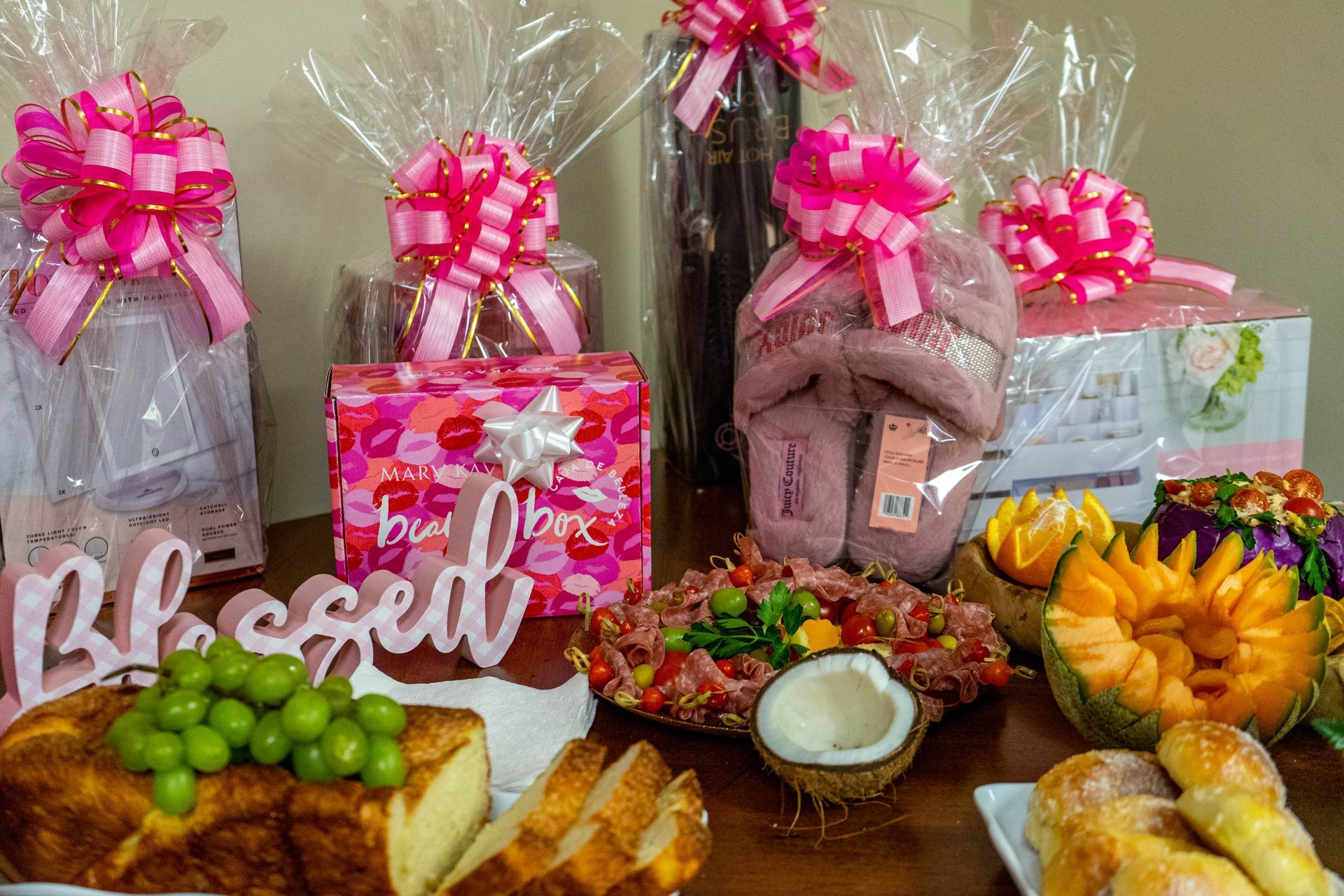 Gift baskets and food items, decorated with pink bows, on a table. Includes
