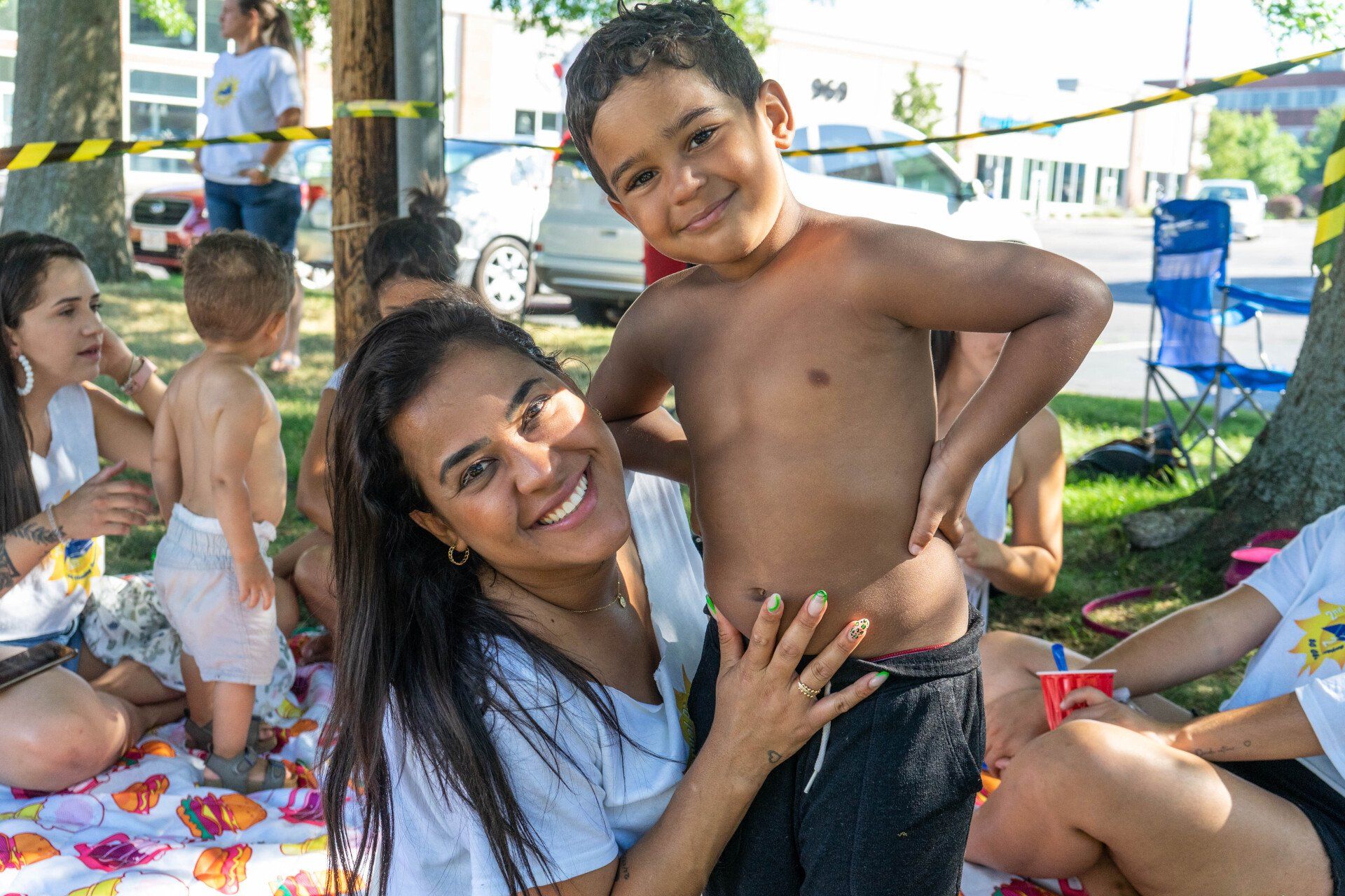 Woman and young boy smiling at the camera outdoors, surrounded by other people and activity.