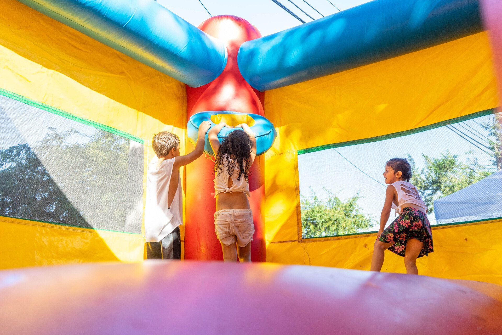 Children playing basketball inside a colorful inflatable bounce house on a sunny day.