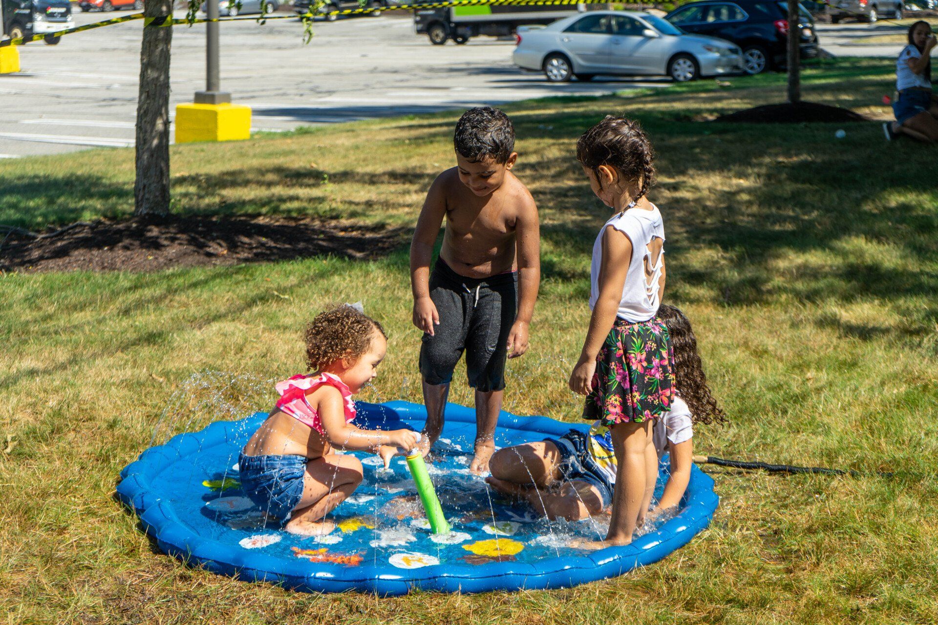 Children playing in a blue splash pad on a grassy area, sunny day.