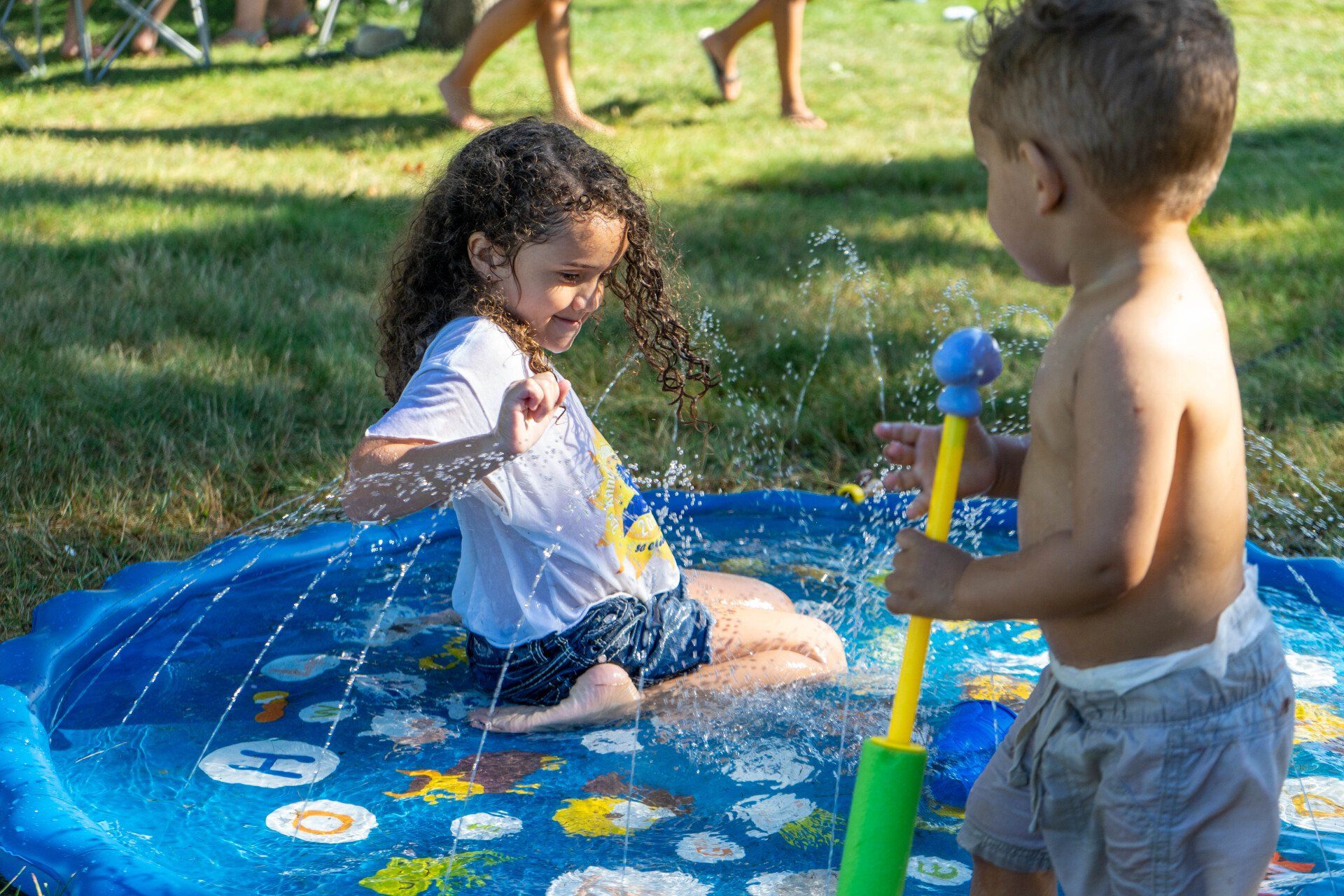 Two children playing in a splash pad in a sunny outdoor setting.