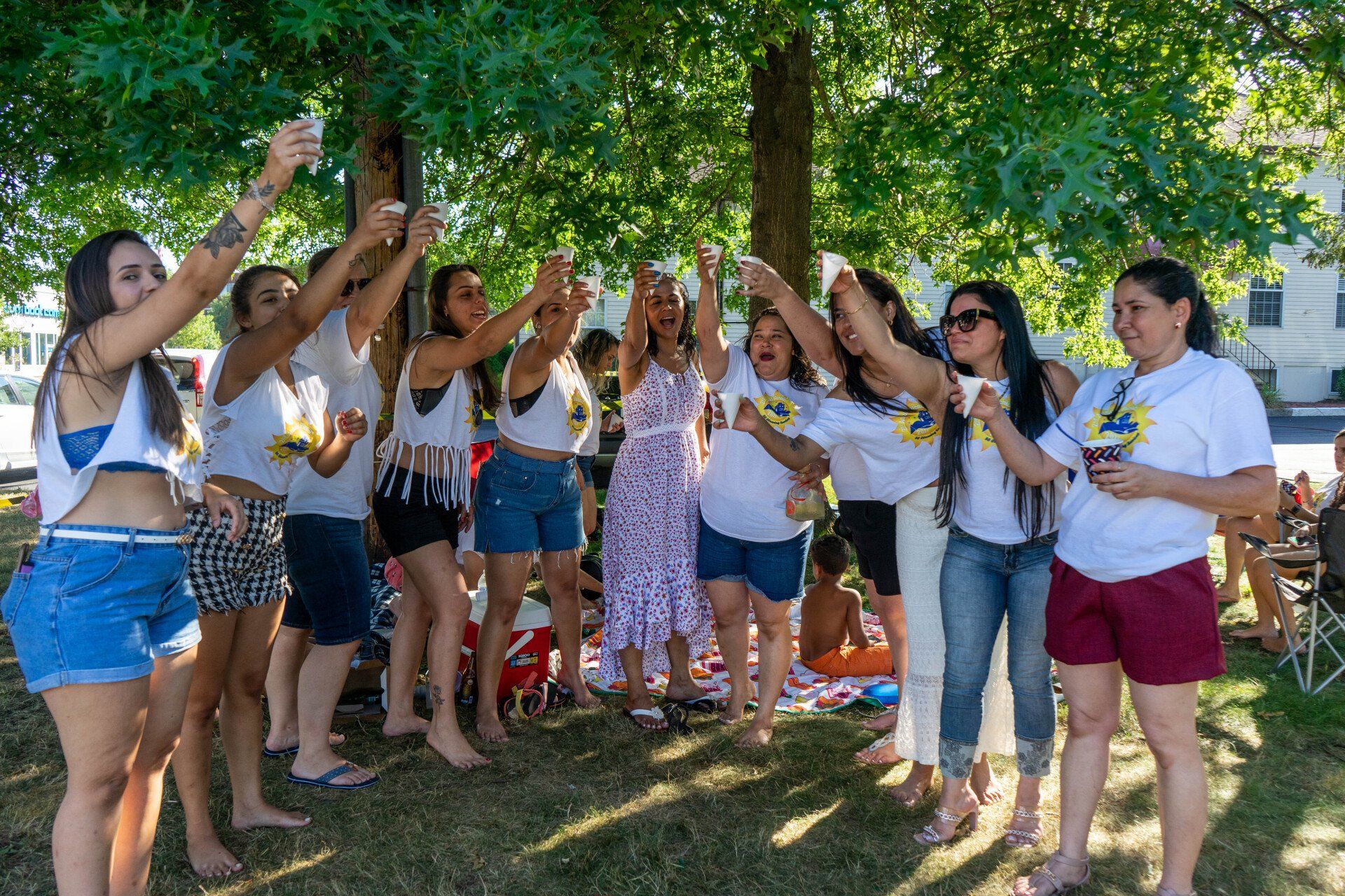 Group of women toasting drinks outdoors under a tree.