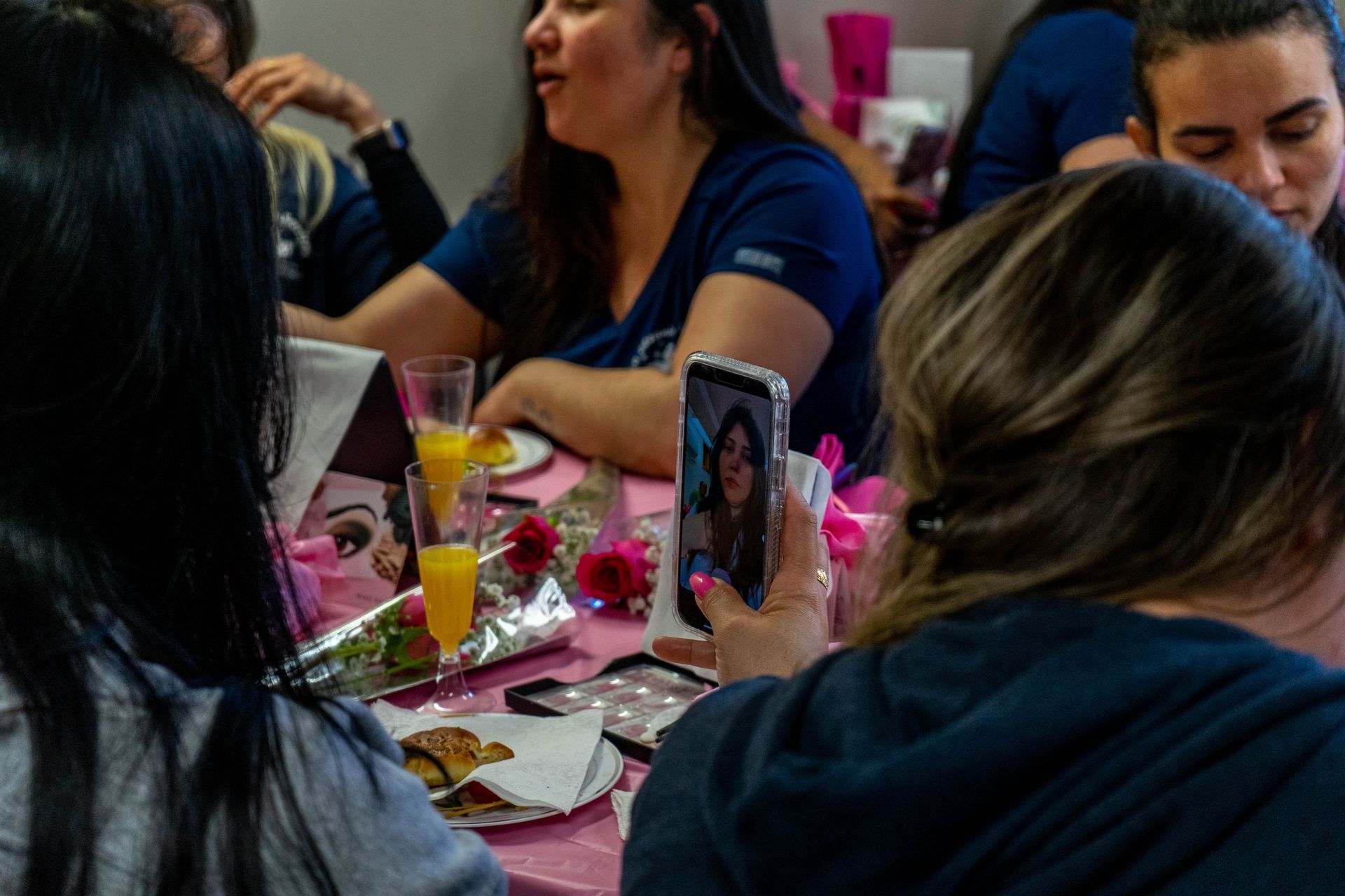 People at a table, one taking a selfie. Table is pink with food and drinks.
