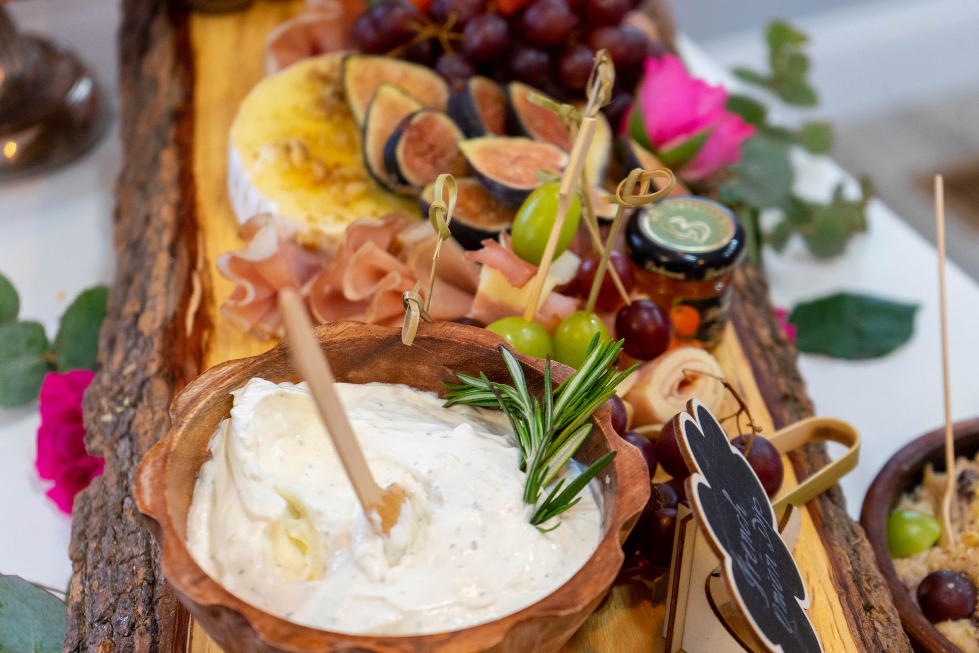 Charcuterie board: cheese, fruit, meat, and dip on a rustic wooden platter.