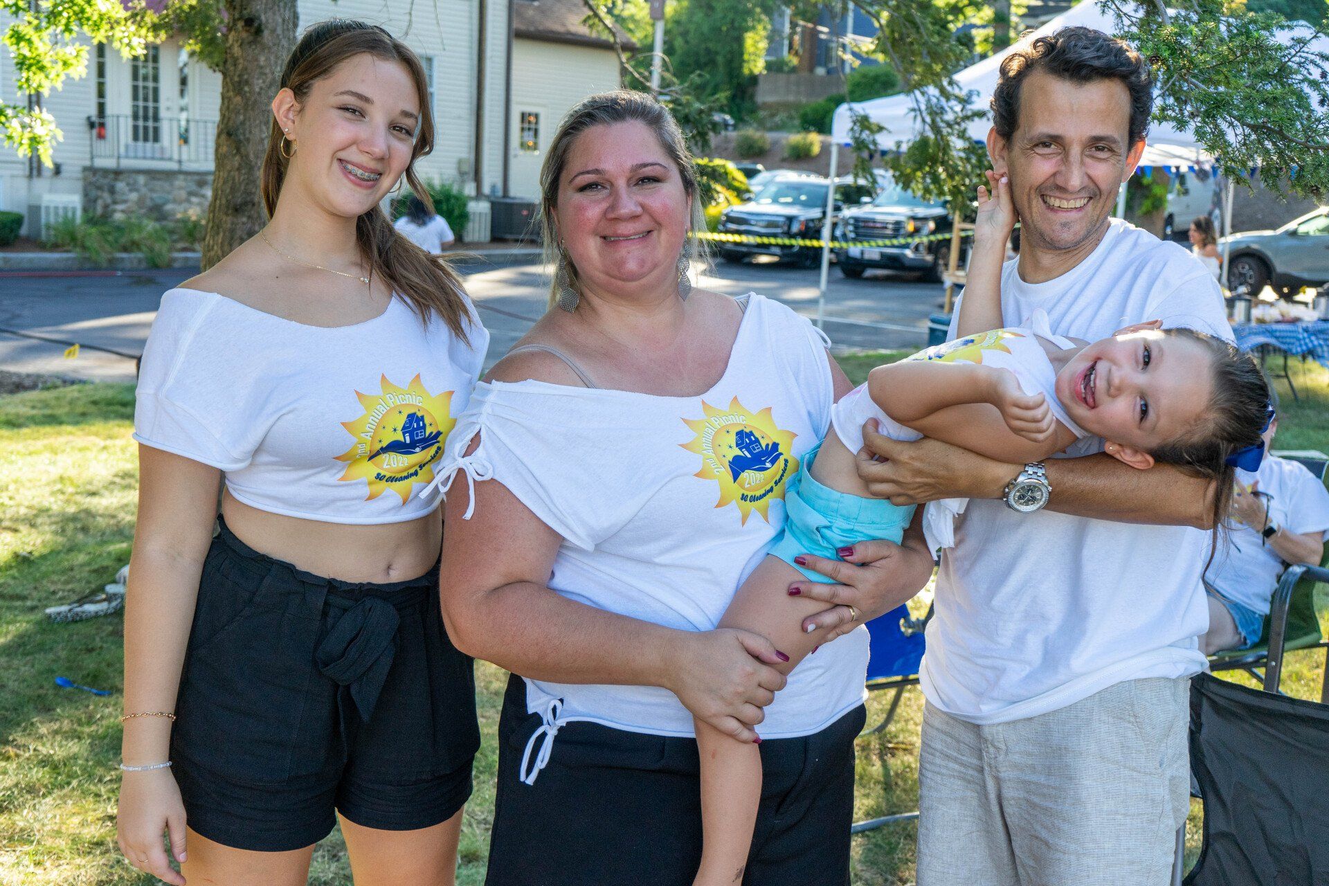 Family of four, wearing matching white shirts with a sun logo, poses outdoors, smiling.