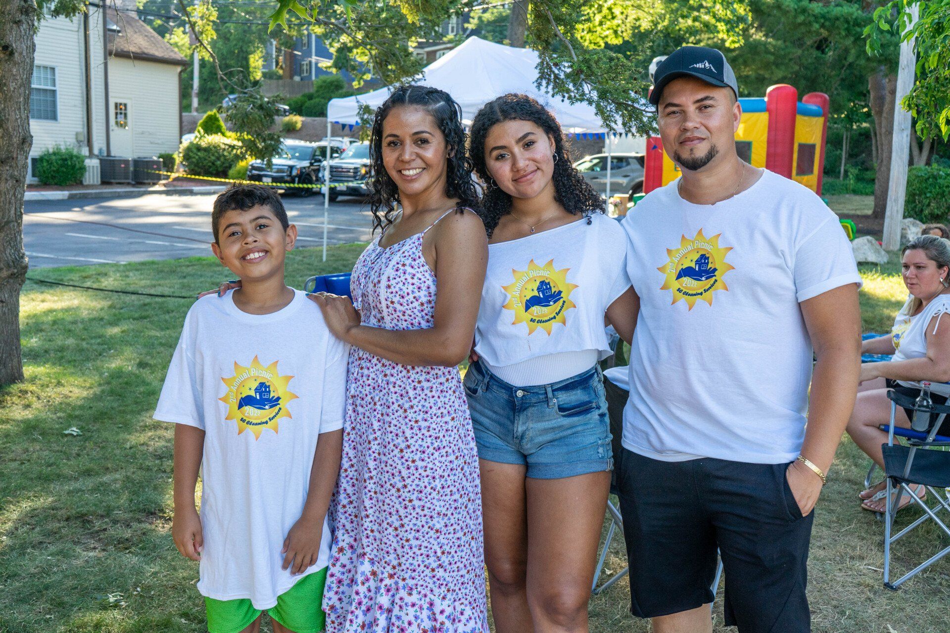 Family of four smiling at a park. They wear matching white shirts with a blue bird logo.