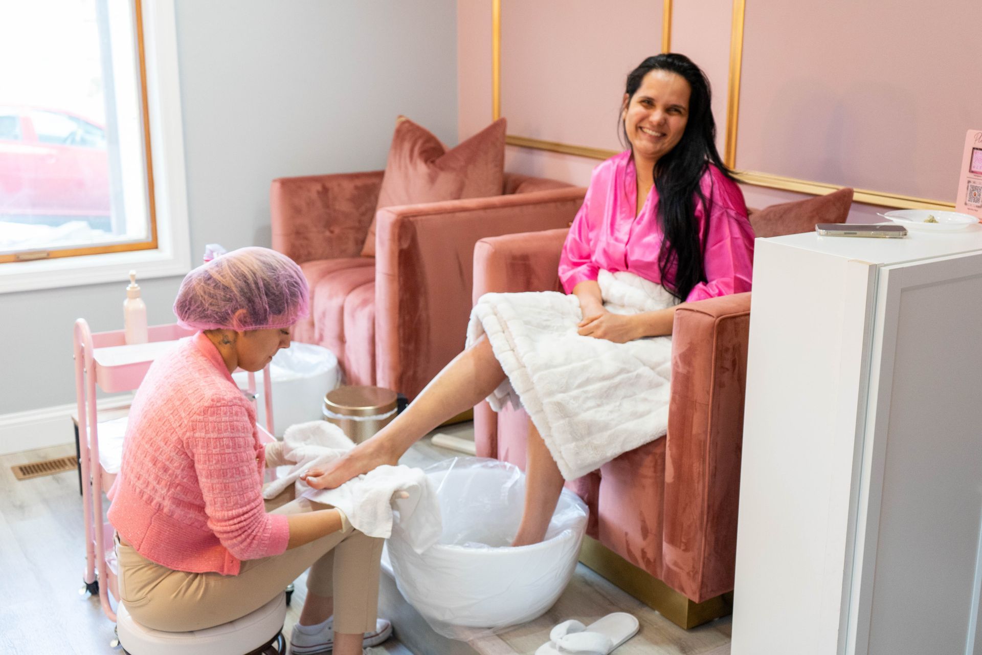 Woman getting a pedicure in a pink salon, smiling, with a technician.