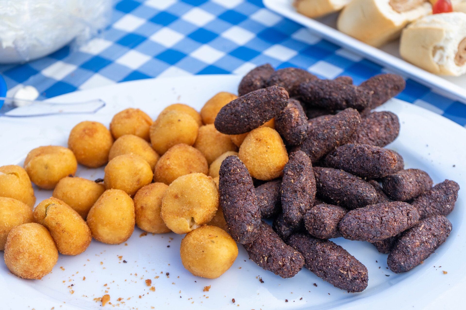 Plate of golden fried balls and dark brown finger foods on a blue checkered cloth.