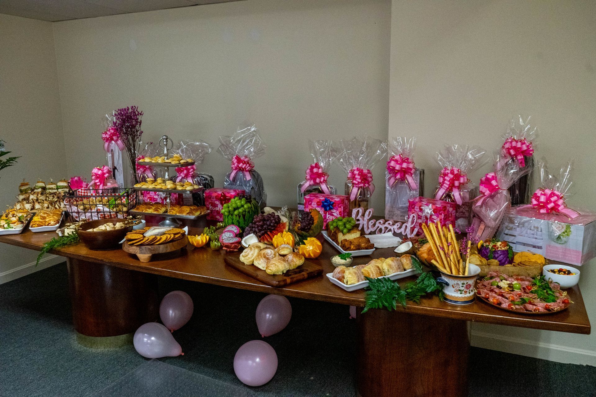 A table laden with food and gift baskets, decorated with pink bows and balloons.