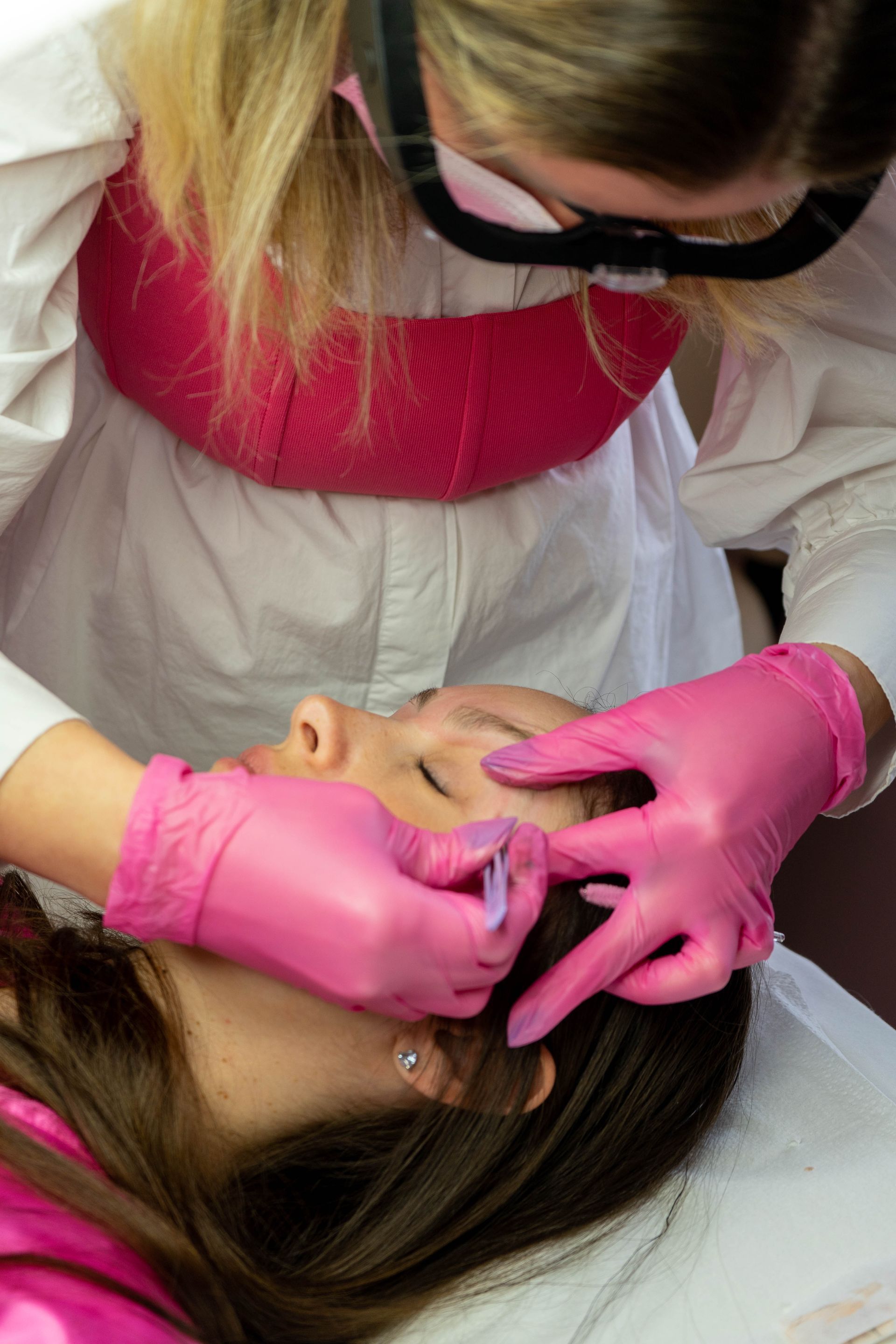 Person in pink gloves injecting a client's face; both are indoors.
