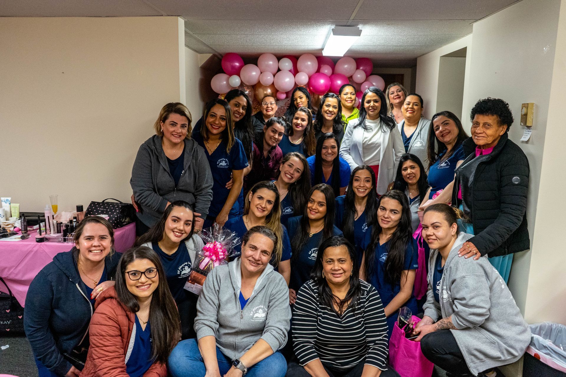 Group of women smiling together, posing with pink balloons in a decorated room.