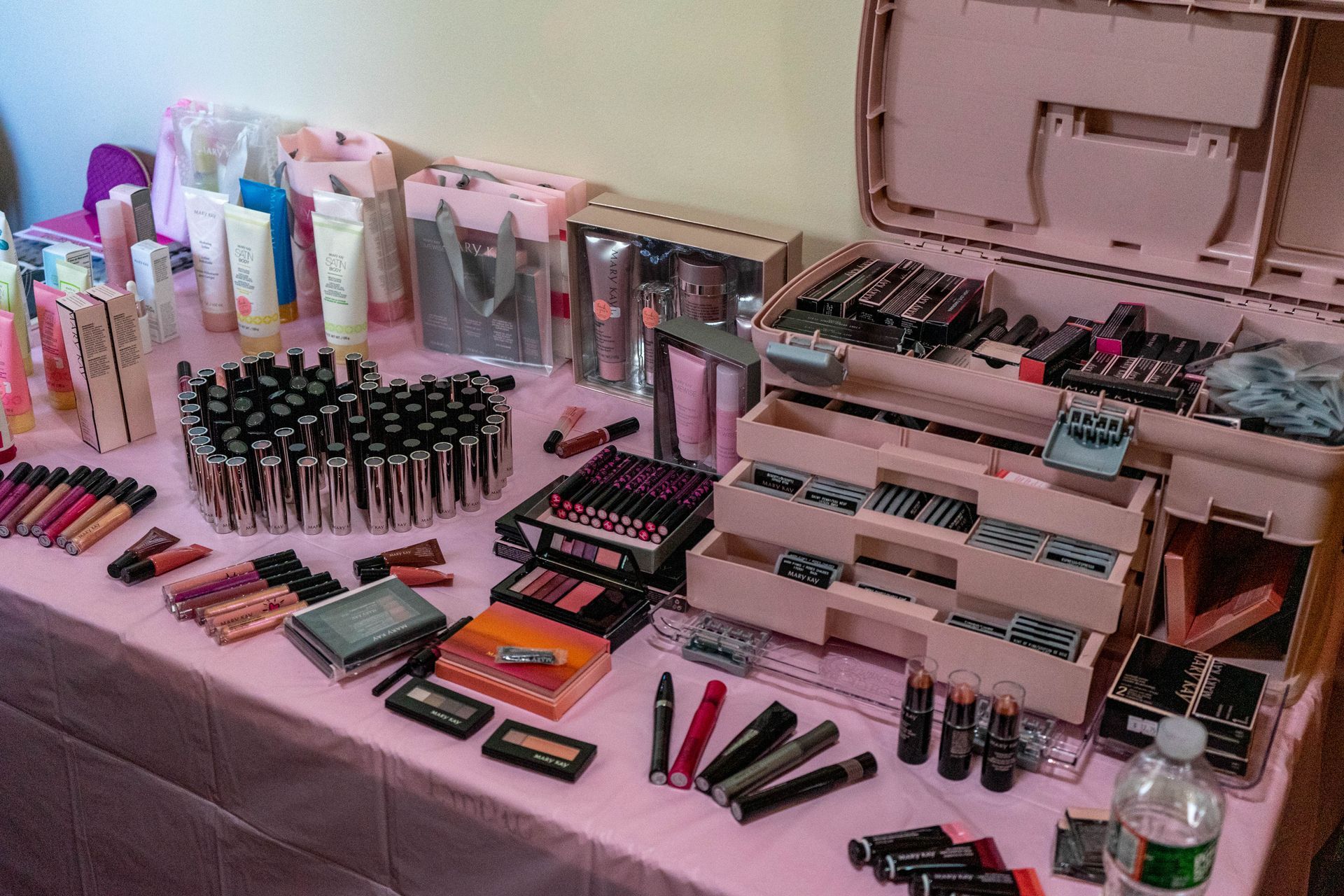 Makeup display on a pink table. Lipsticks, palettes, and skincare products are arranged in a store setting.