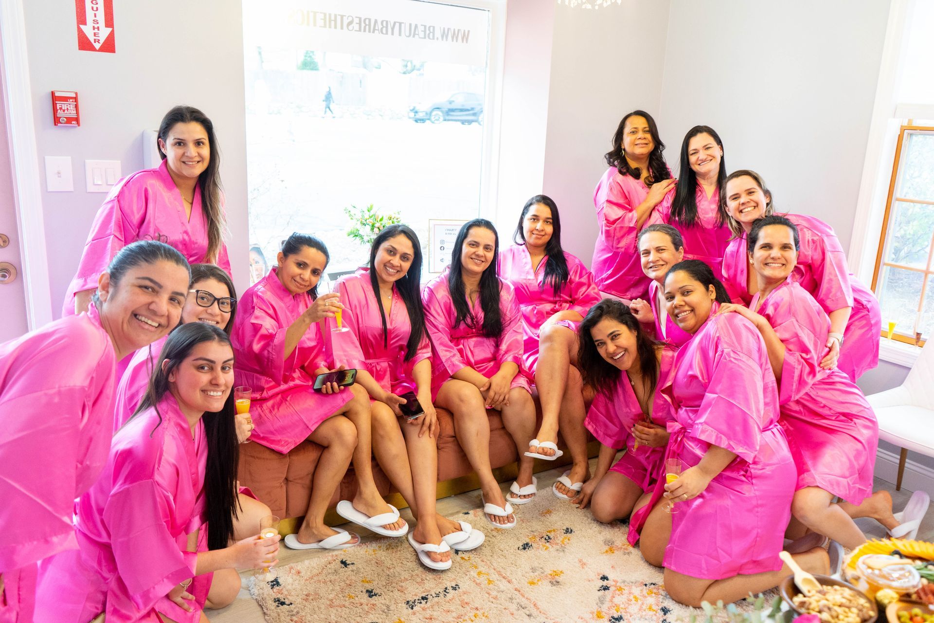 Group of women in pink robes smiling, relaxing, and posing together in a brightly lit room.