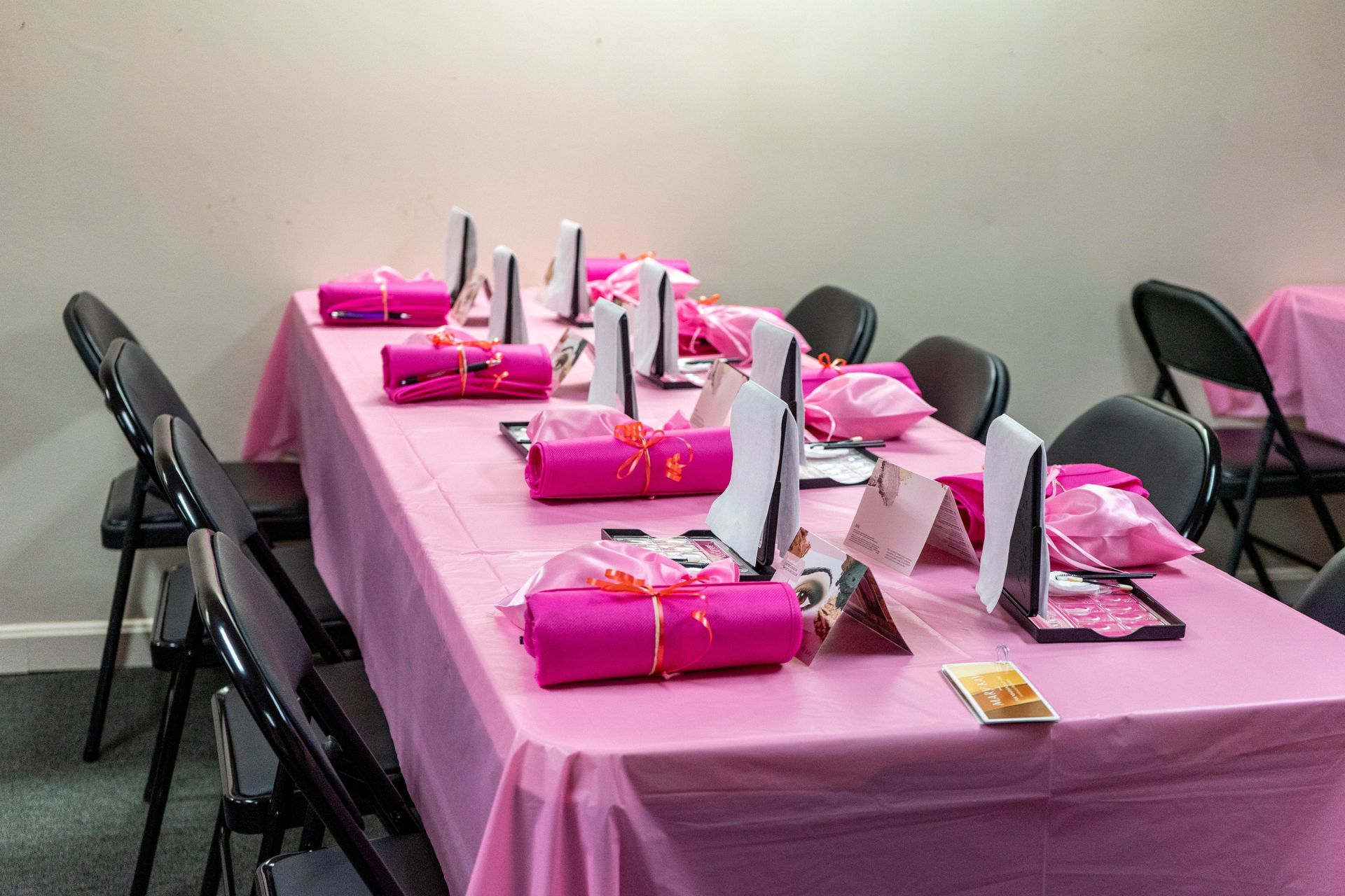 A table set for a party with pink tablecloth, gifts, cards, and black chairs.