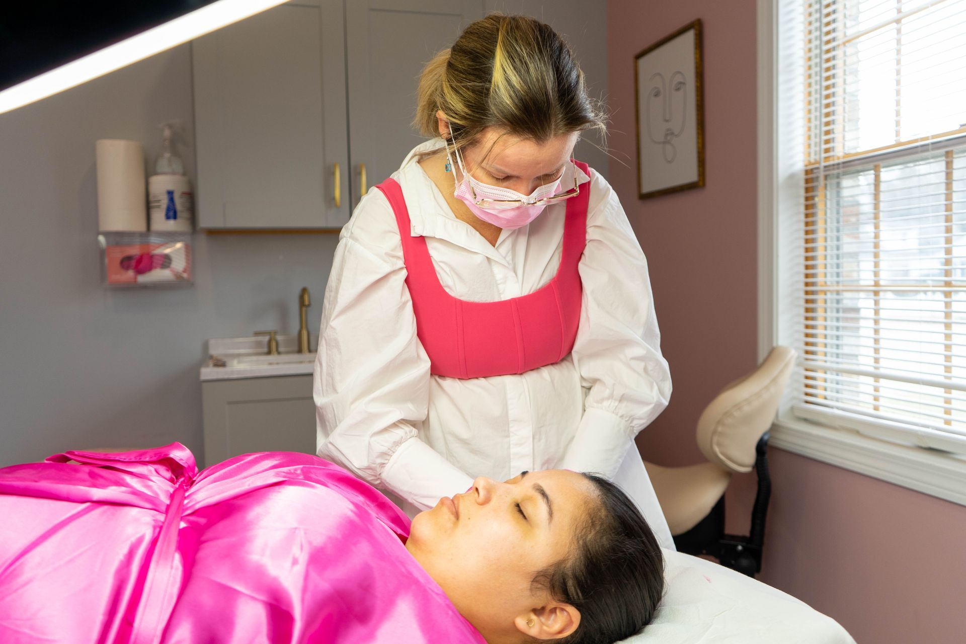 Woman receiving facial treatment in a pink-themed spa setting.