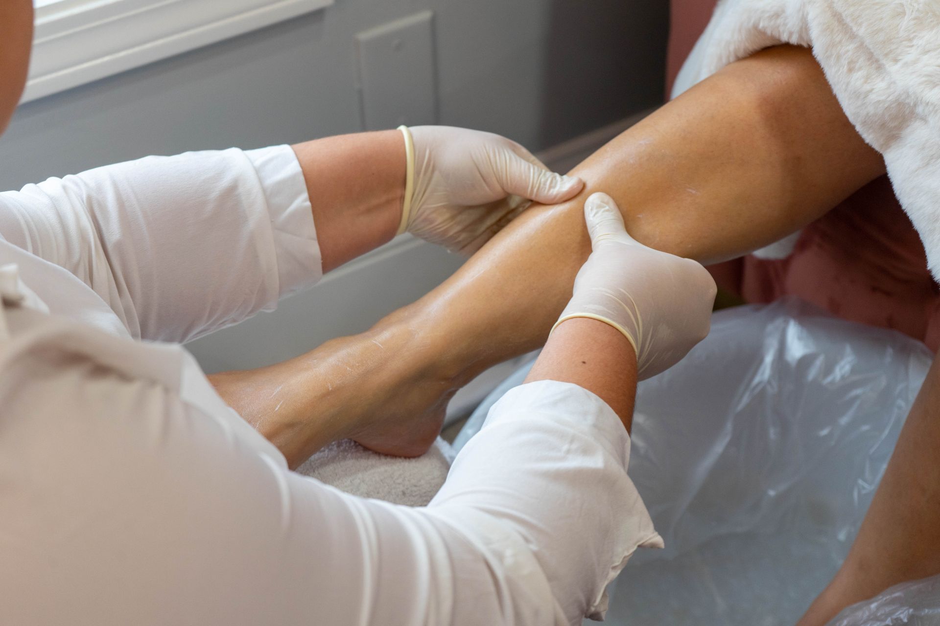 Person in white gloves massaging another person's leg, in a spa-like setting.