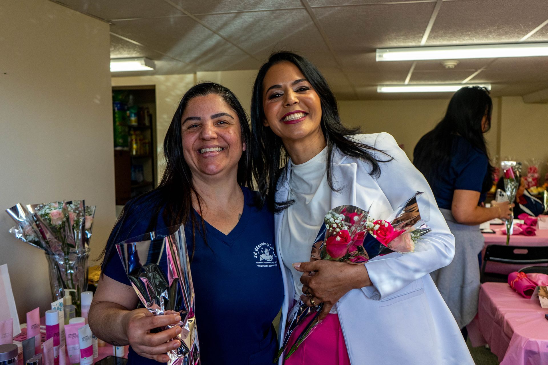 Two smiling women holding flowers, one in scrubs, the other in a white coat.
