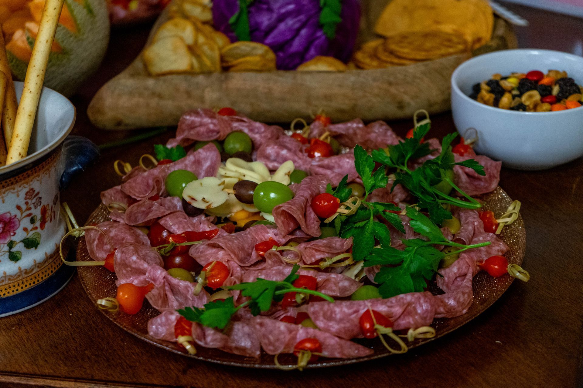 A platter of salami, olives, cherry tomatoes, and parsley arranged on a table for an appetizer.