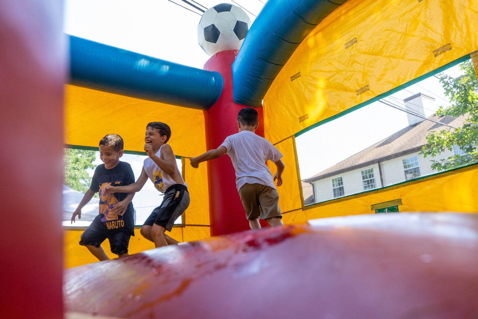 Three young boys playing in a soccer-themed inflatable bounce house on a sunny day.