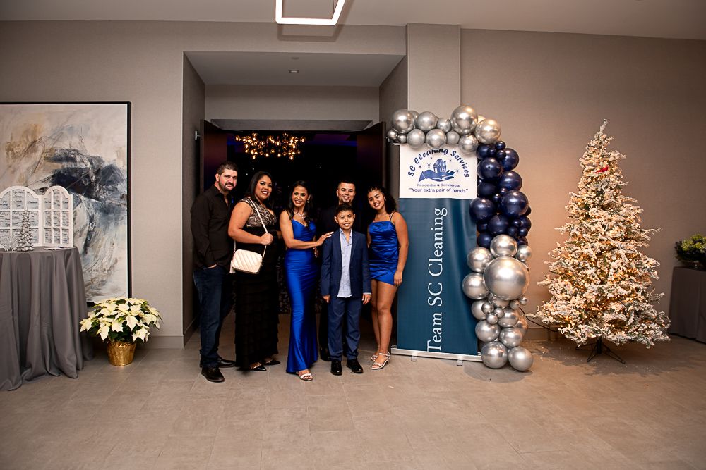 Family poses at an event with balloons, banner, and Christmas tree.