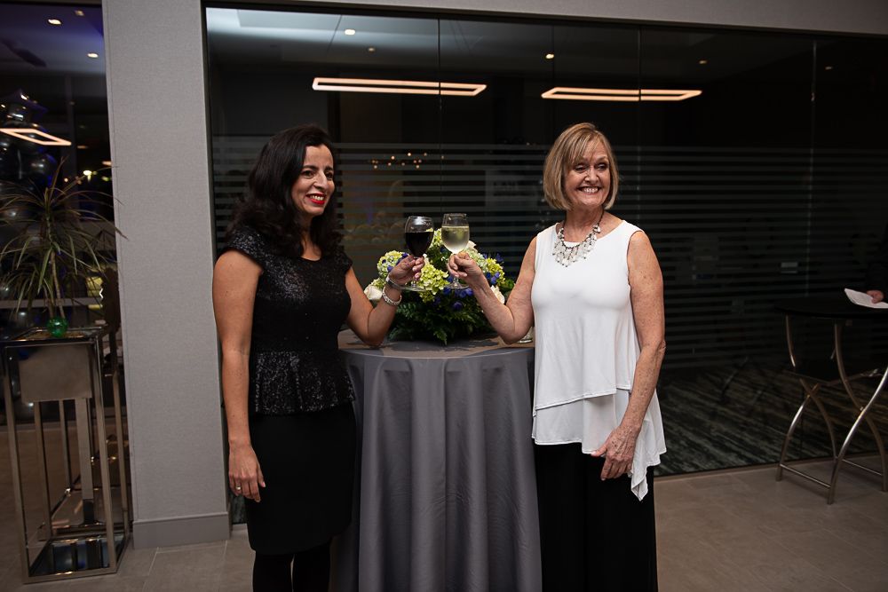 Two women in formal attire toasting with wine glasses at an event.