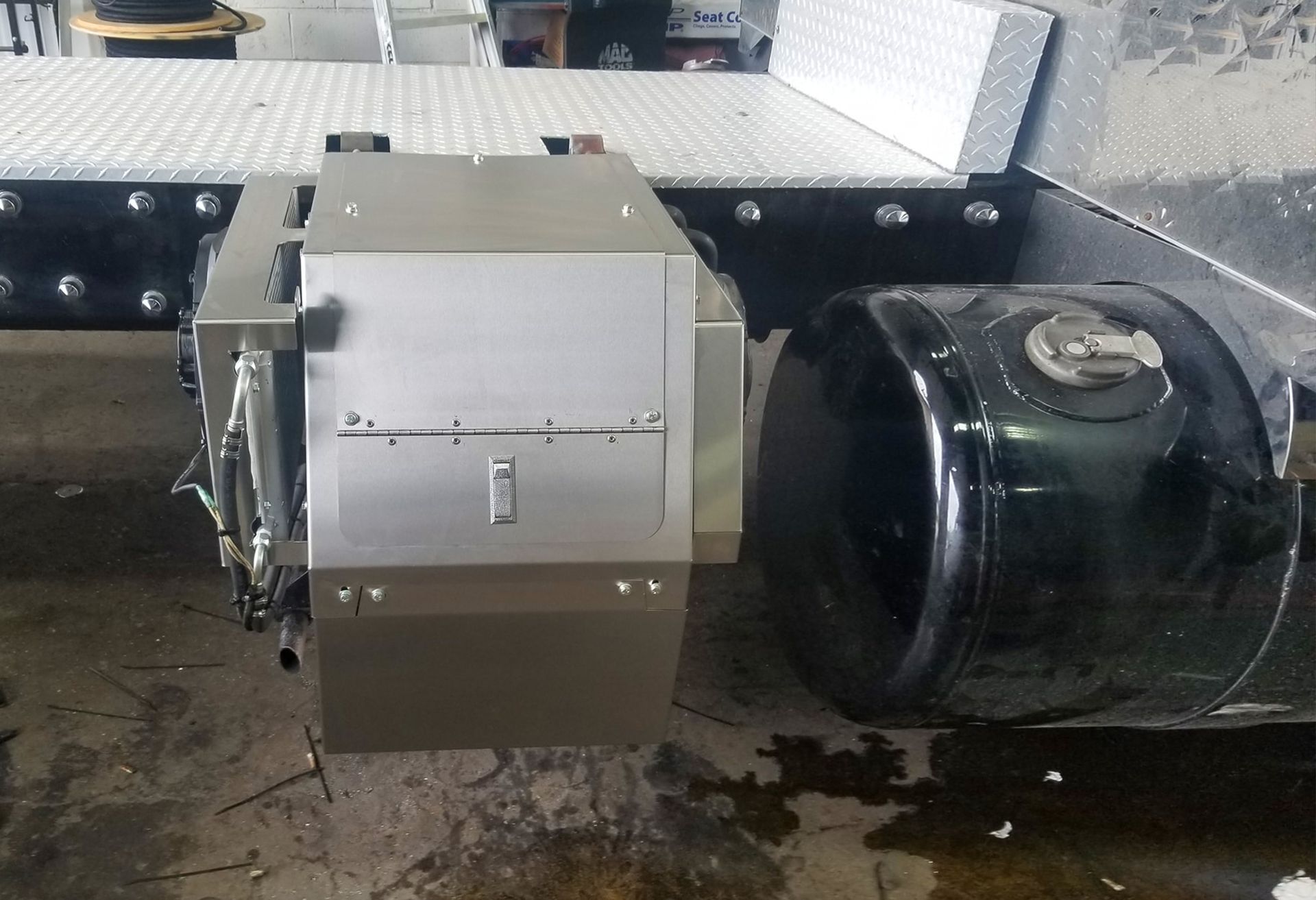 Industrial machinery with a silver box attached to a large black cylindrical drum on a metal platform, with a wet floor below.