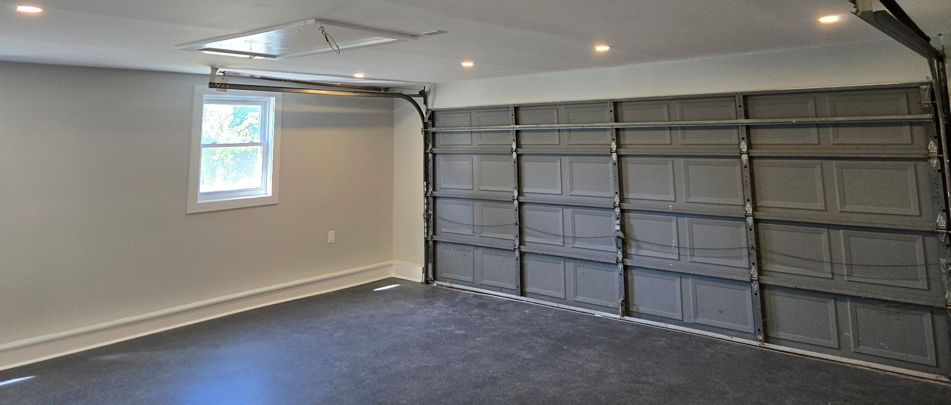 Empty garage interior with gray walls, recessed lights, small window, and closed garage door