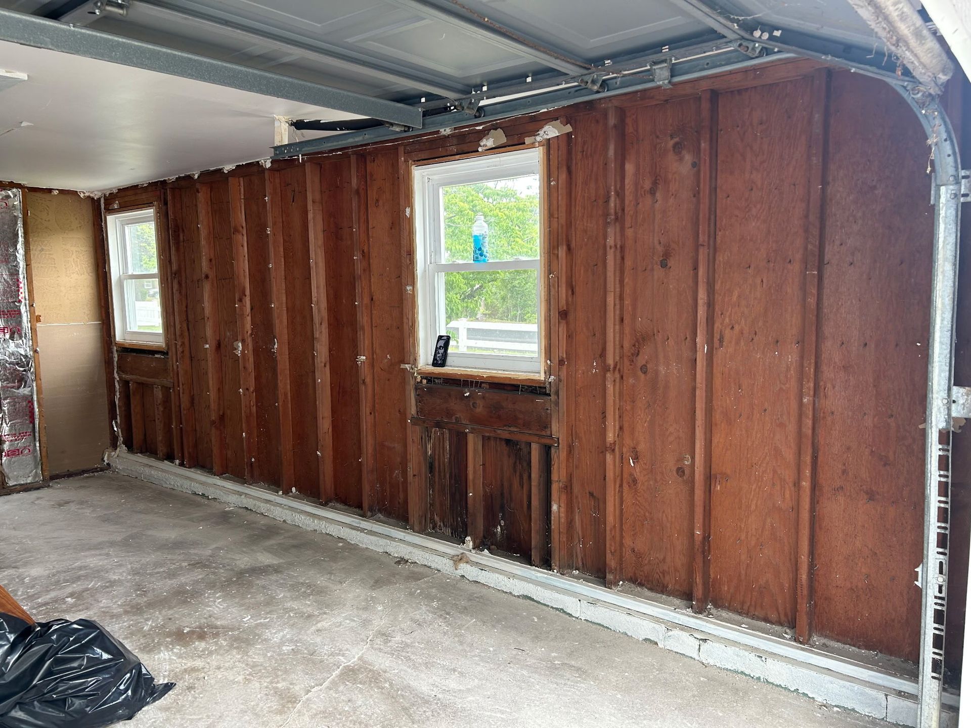 Partially finished garage interior with wood-paneled wall, window, and concrete floor