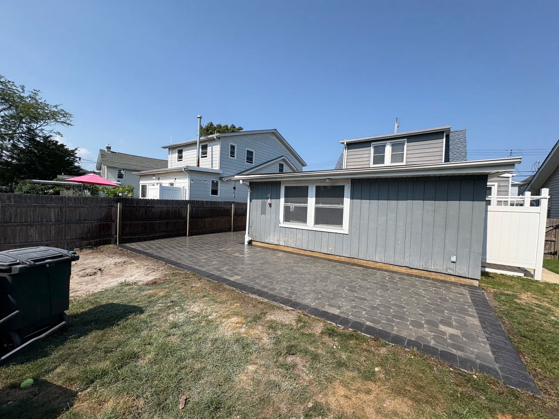 Backyard with a gray shed, gravel path, grass, and fenced neighboring houses under a blue sky