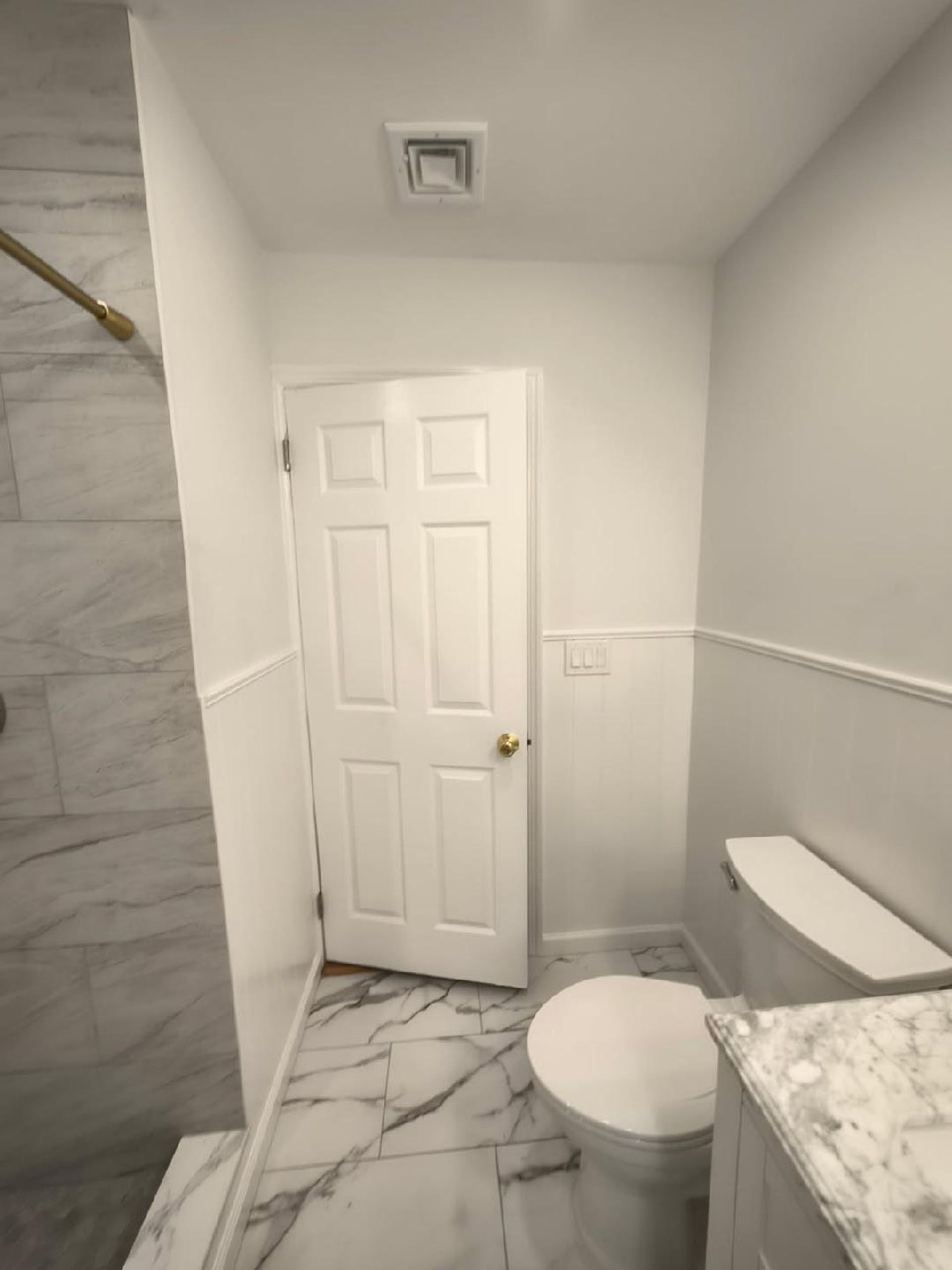 Bathroom with white marble tile floor, white toilet, and door.